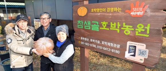 최 대표 부부가 아들 정환(왼쪽)씨와 농원 입구에서 호박을 들어 보이고 있다.