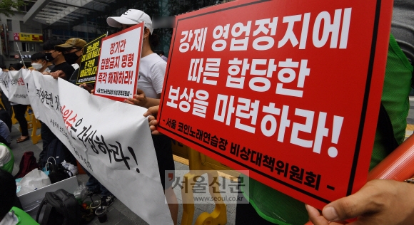 29일 서울 중구 서울시청 서소문2청사 앞에서 열린 서울 지역 코인노래방 집합금지명령 해제 촉구 집회에서 코인노래연습장 비상대책위원회 회원들이 ‘강제 영업정지에 따른 합당한 보상을 마련하라’ 등의 문구가 쓰인 피켓을 들고 있다. 오장환 기자 5zzang@seoul.co.kr