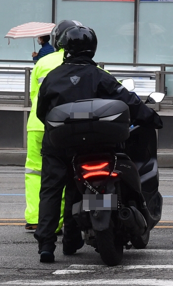 카메라를 발견하고 황급히 오토바이에서 내려 오토바이를 끌고 가는 운전자. 번호판은 일명 순대라 불리는 자물쇠로 가려 놨다.