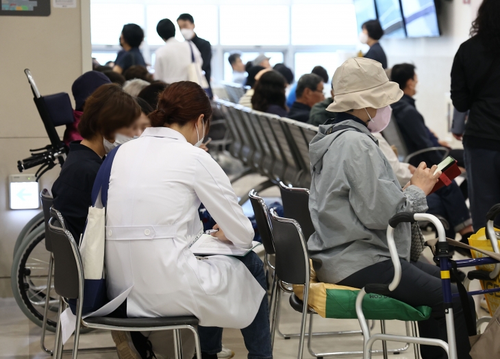 지난 22일 서울의 한 대학병원 진료실 앞에서 한 의사가 대기 중인 환자에게 다가가 진료를 보고 있다. 연합뉴스 지난 22일 서울의 한 대학병원 진료실 앞에서 한 의사가 대기 중인 환자에게 다가가 진료를 보고 있다. 연합뉴스
