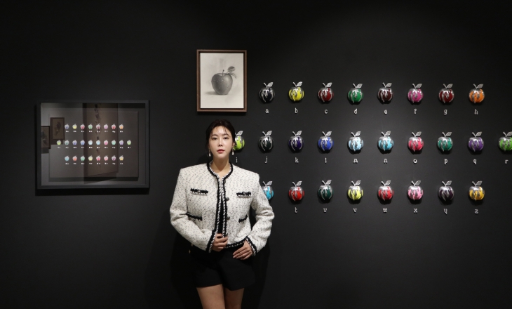 가수 겸 화가 권지안(솔비)이 최근 서양화가 윤위동과의 2인전을 통해 선보인 자신의 부조 작품 ‘애플’ 시리즈와 윤위동의 사과 연필 소묘(머리 위)가 함께 걸린 벽 앞에 서 있다. 지안캐슬 제공