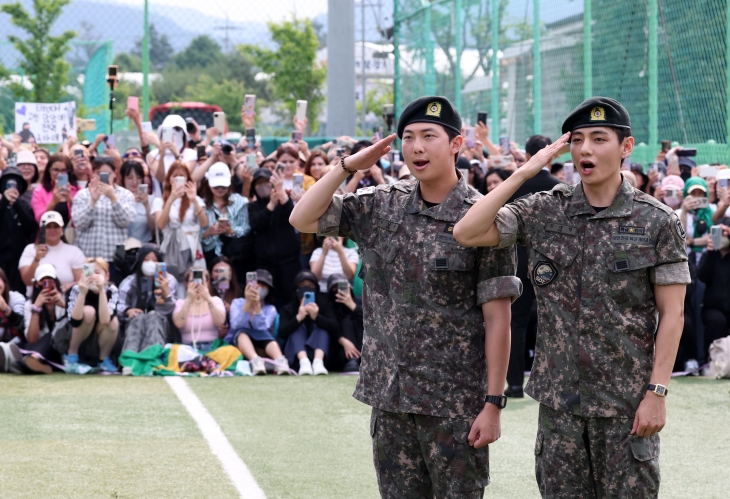 10일 군 복무를 마친 방탄소년단(BTS)의 RM(왼쪽)과 뷔가 강원 춘천 신북읍체육공원 축구장에서 팬들에게 거수경례하며 전역 신고를 하고 있다. 춘천 연합뉴스